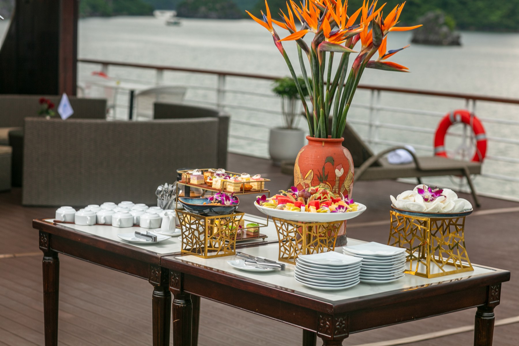 Afternoon tea table on the Sundeck of Hermes Premium with a fruit platter and cakes beside a lifebuoy