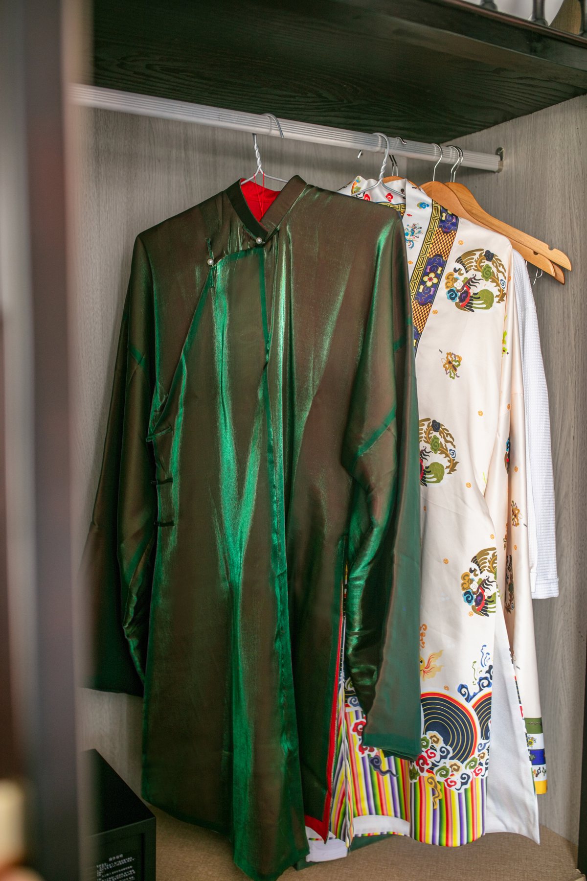 Ao Dai dresses hanging in a wardrobe on Hermes Premium, one green and one white with colorful embroidery
