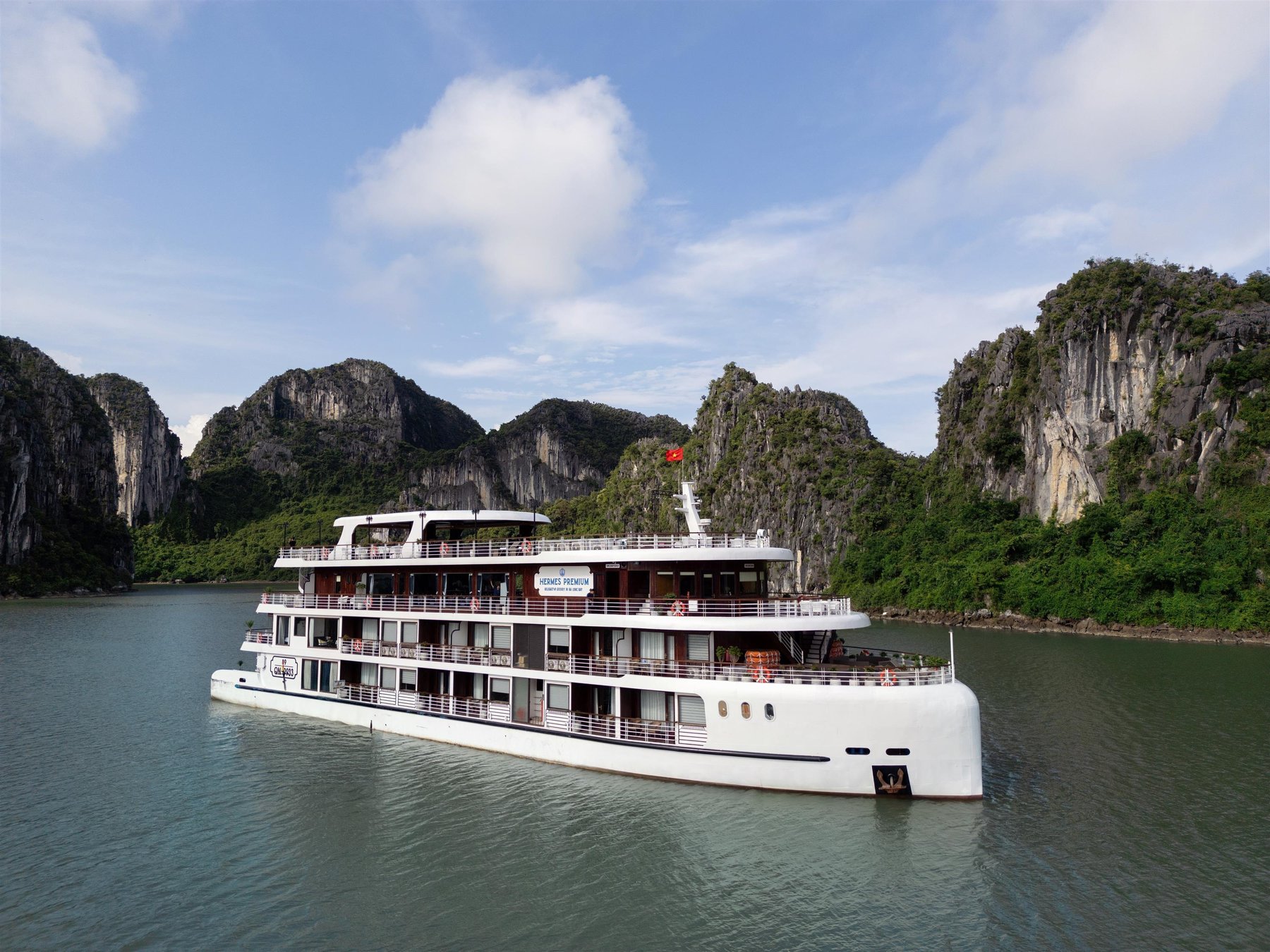 Hermes Premium cruise ship seen from the water with limestone cliffs behind it in Halong Bay