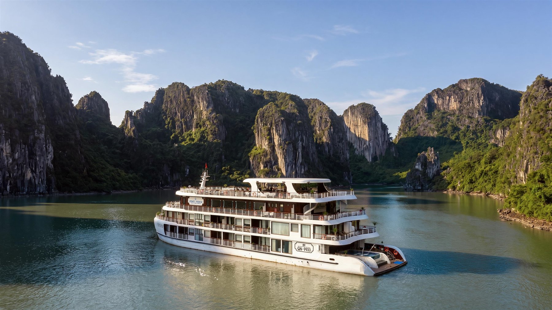 Tall grey limestone towers covered in green forest rising beside calm water in Halong Bay
