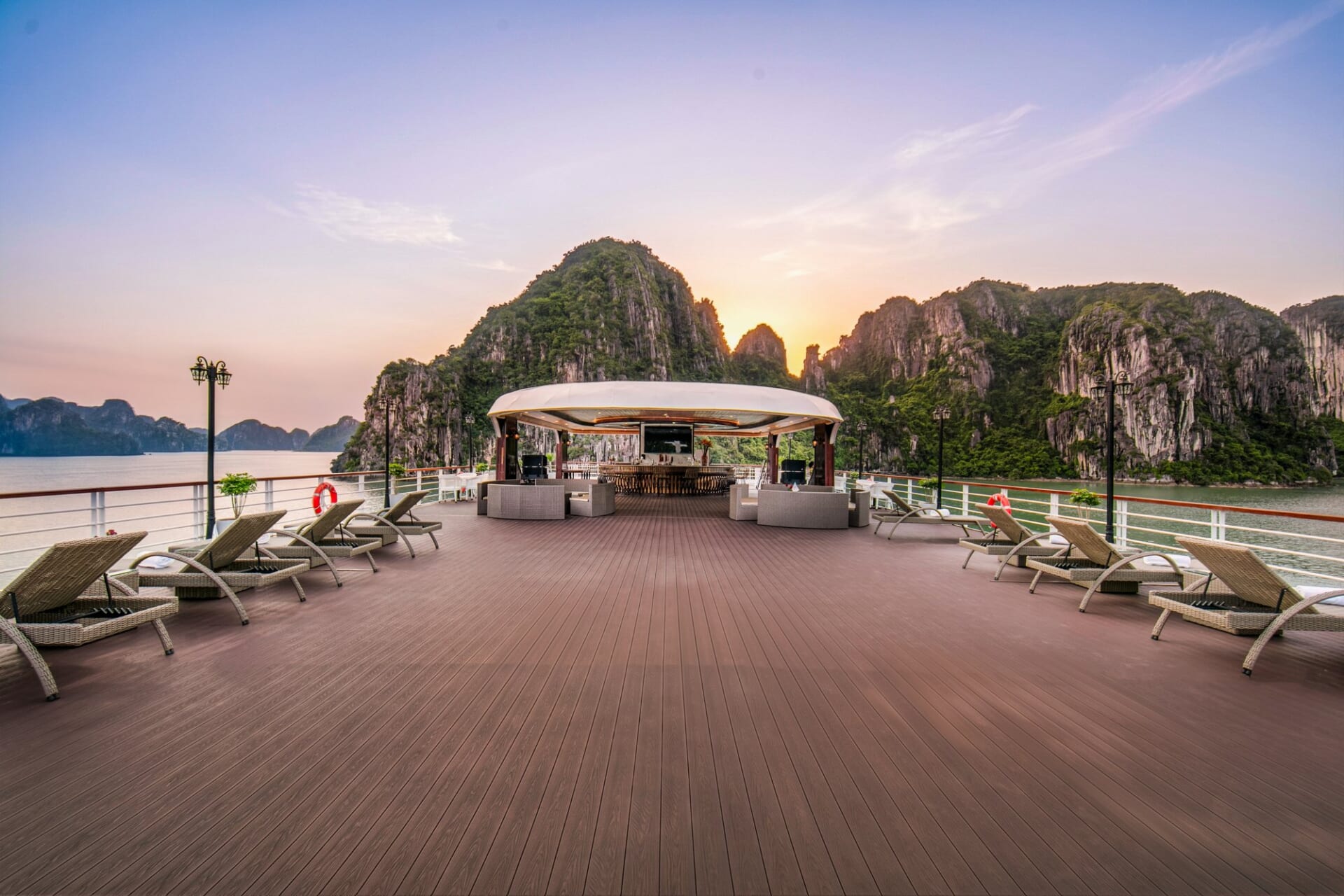 Sundeck of Hermes Premium with sun loungers and a bar pavilion under a pink evening sky